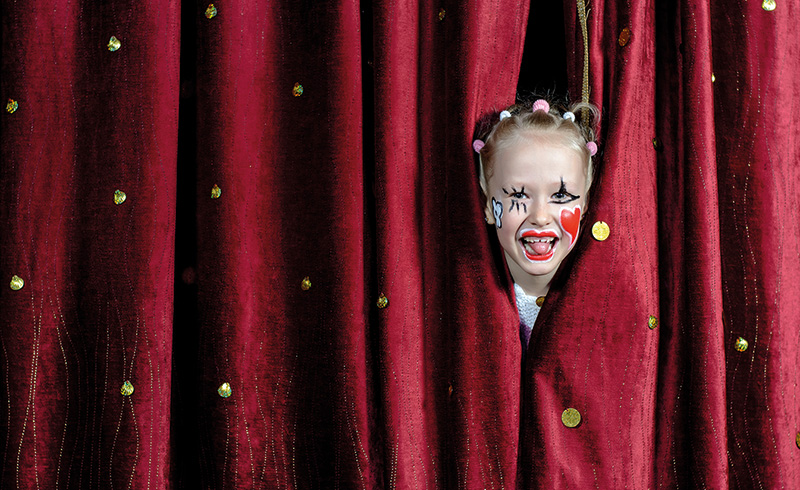 Der Kopf eines Kindes schaut durch den Spalt eines Theatervorhangs